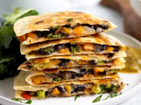 Golden brown collard greens and black bean quesadilla cut into wedges on a rustic wooden cutting board, garnished with fresh cilantro and served with lime wedges and salsa