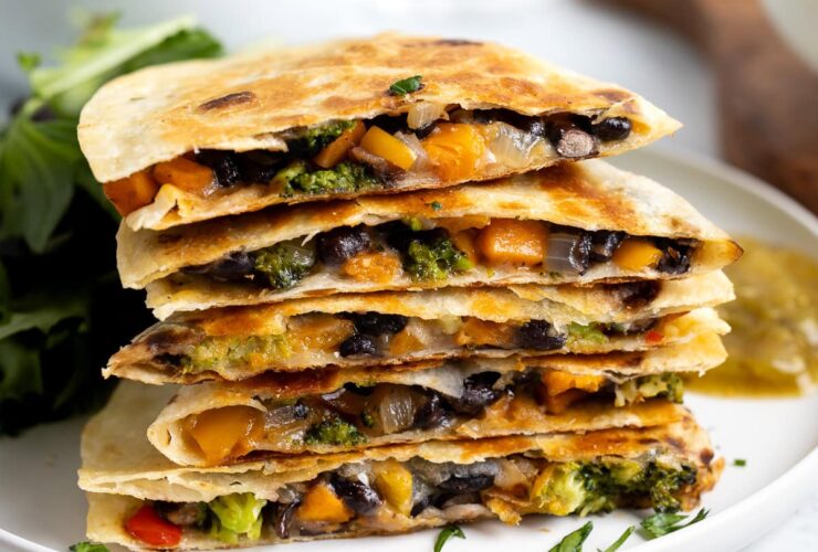 Golden brown collard greens and black bean quesadilla cut into wedges on a rustic wooden cutting board, garnished with fresh cilantro and served with lime wedges and salsa