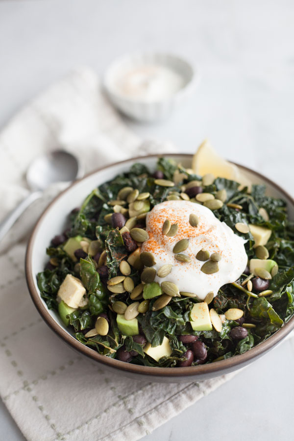 Collard greens being sautéed in a skillet alongside black beans and spices, with ingredients laid out nearby including shredded cheese and tortillas