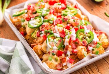 loaded tater tot nachos on large platter with melted cheese, ground beef, jalapeños, and fresh toppings