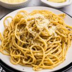 Perfectly plated cacio e pepe pasta with freshly cracked black pepper and grated pecorino romano cheese, photographed from above with golden lighting