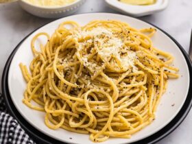 Perfectly plated cacio e pepe pasta with freshly cracked black pepper and grated pecorino romano cheese, photographed from above with golden lighting