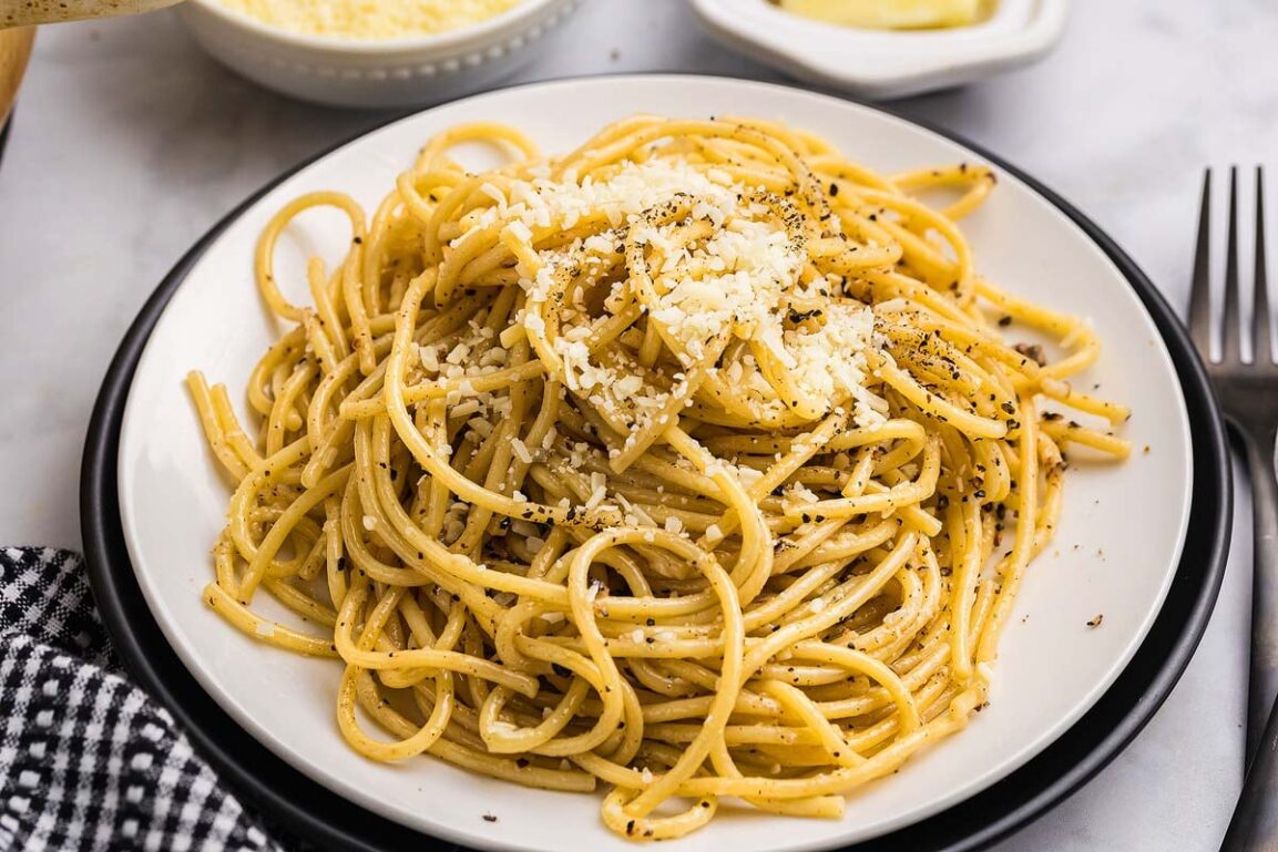 Perfectly plated cacio e pepe pasta with freshly cracked black pepper and grated pecorino romano cheese, photographed from above with golden lighting