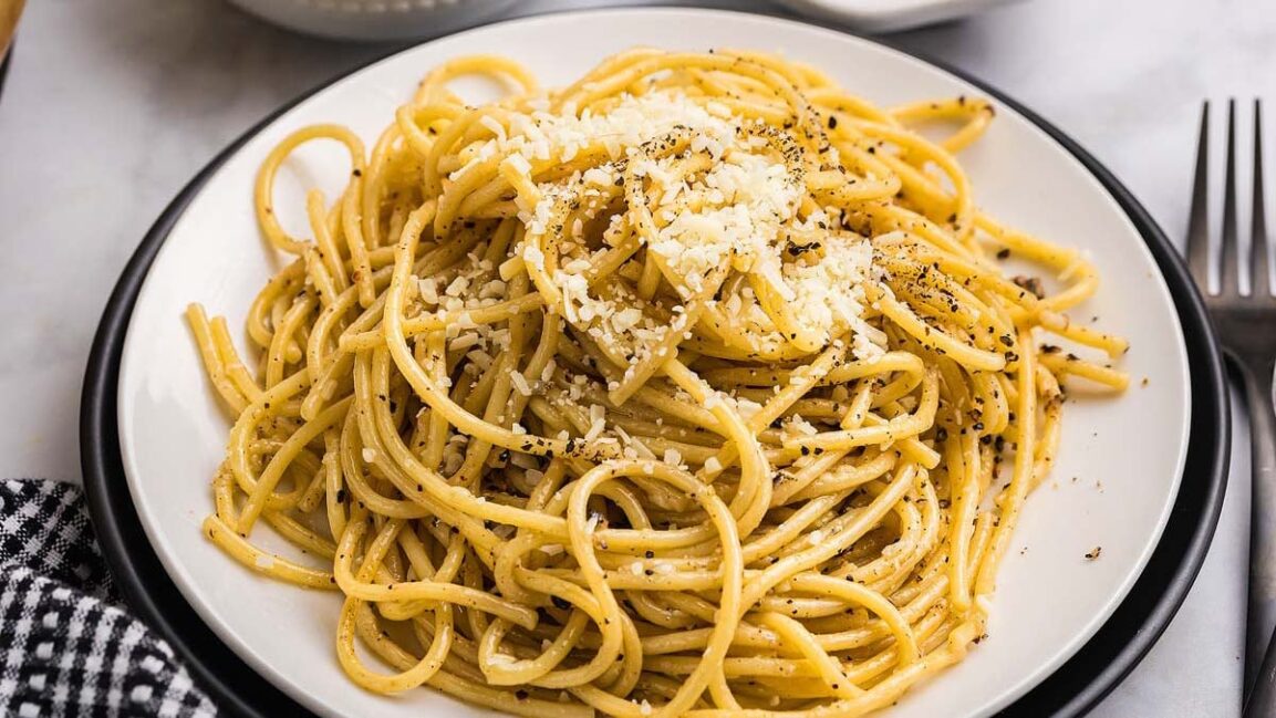 Close-up shot of creamy cacio e pepe pasta twirled on a fork, showing the glossy sauce coating and black pepper specks