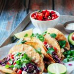 Perfectly grilled carne asada tacos on warm corn tortillas with fresh cilantro, diced onions, and lime wedges, beautifully plated on a rustic wooden board