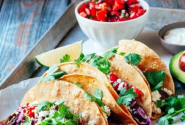 Perfectly grilled carne asada tacos on warm corn tortillas with fresh cilantro, diced onions, and lime wedges, beautifully plated on a rustic wooden board