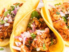 Chicken tinga served on warm tortillas with fresh cilantro, diced onions, and lime wedges, showing the rich reddish-brown sauce coating tender shredded chicken