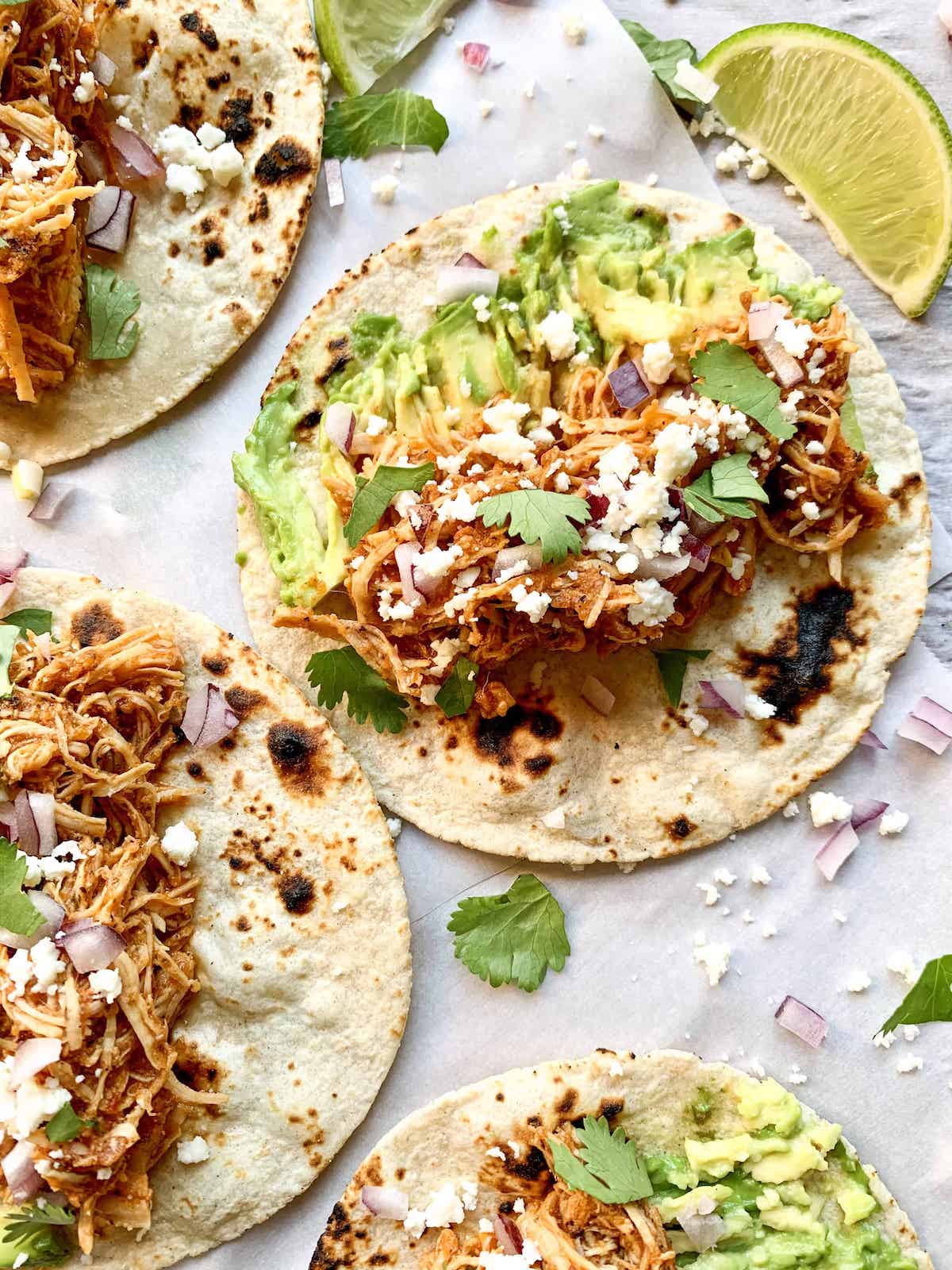 Close-up shot of chicken tinga in a warm tortilla garnished with fresh white onions, cilantro, and a lime wedge, showing the rich texture and color of the shredded chicken