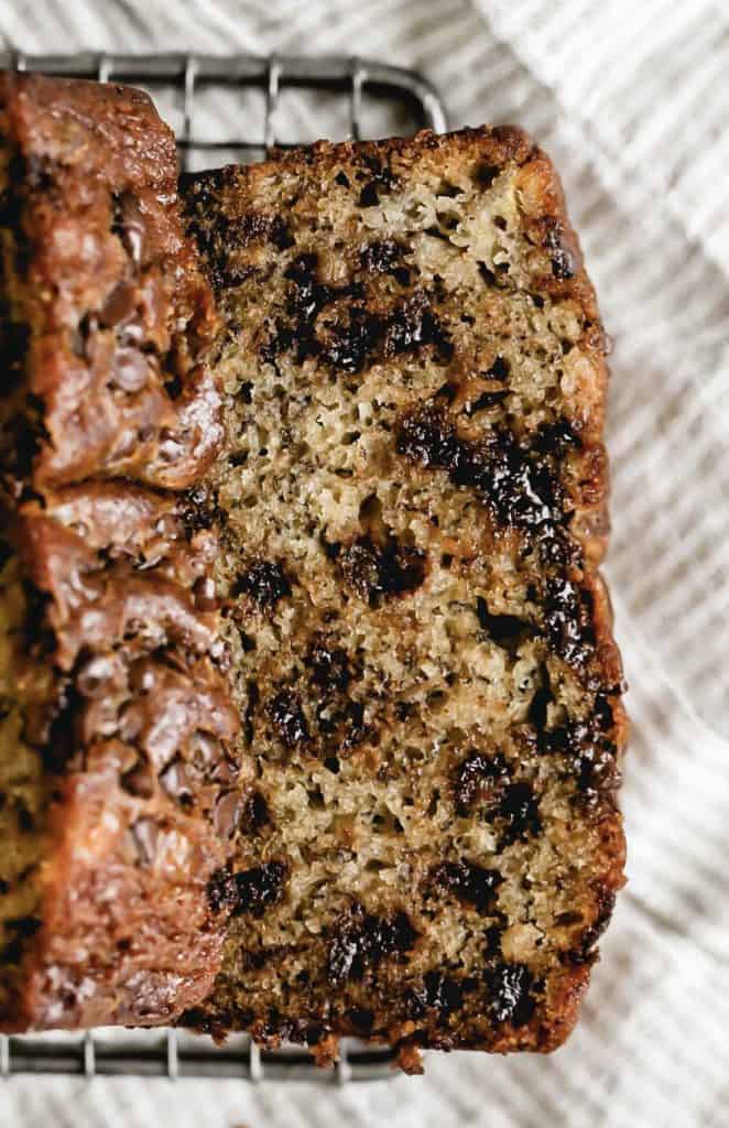 Close-up slice of chocolate chunk banana bread on white plate showing moist crumb texture with melted chocolate chunks, fork beside plate