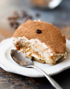 Classic tiramisu slice on elegant white plate showing distinct layers with cocoa powder dusting