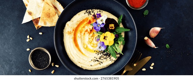 Perfectly smooth creamy hummus in a wide shallow bowl, drizzled with golden olive oil and garnished with paprika, chickpeas, and fresh herbs, photographed from above on a rustic wooden table
