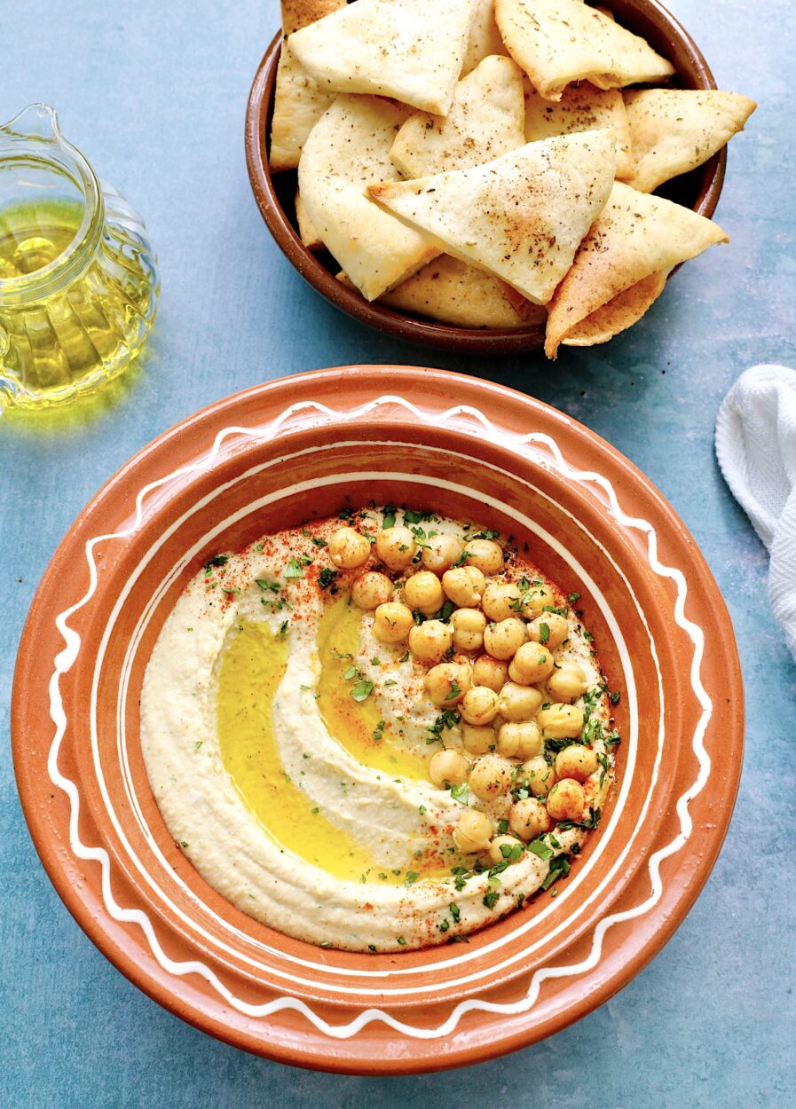 Close-up shot of creamy hummus being scooped with warm pita bread, showing the perfect smooth texture and golden olive oil drizzle