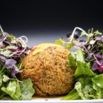 Golden crispy falafel balls arranged on a rustic wooden platter with fresh herbs, tahini drizzle, and colorful vegetables
