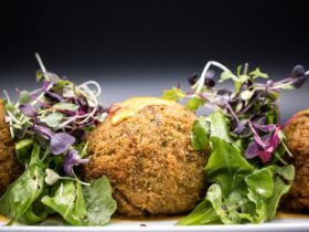 Golden crispy falafel balls arranged on a rustic wooden platter with fresh herbs, tahini drizzle, and colorful vegetables