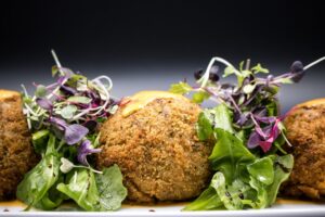Golden crispy falafel balls arranged on a rustic wooden platter with fresh herbs, tahini drizzle, and colorful vegetables
