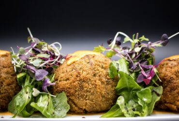 Golden crispy falafel balls arranged on a rustic wooden platter with fresh herbs, tahini drizzle, and colorful vegetables