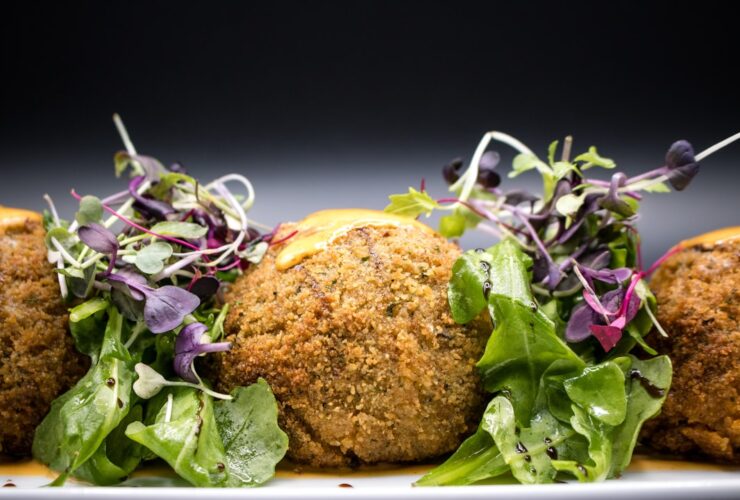 Golden crispy falafel balls arranged on a rustic wooden platter with fresh herbs, tahini drizzle, and colorful vegetables