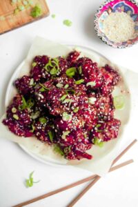 Korean fried chicken pieces glistening with glossy red glaze arranged on a white platter with sesame seeds and scallions