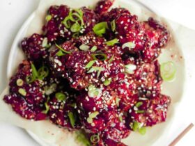 Korean fried chicken pieces glistening with glossy red glaze arranged on a white platter with sesame seeds and scallions