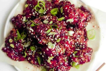 Korean fried chicken pieces glistening with glossy red glaze arranged on a white platter with sesame seeds and scallions