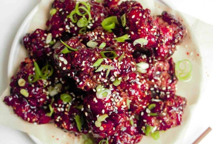 Korean fried chicken pieces glistening with glossy red glaze arranged on a white platter with sesame seeds and scallions