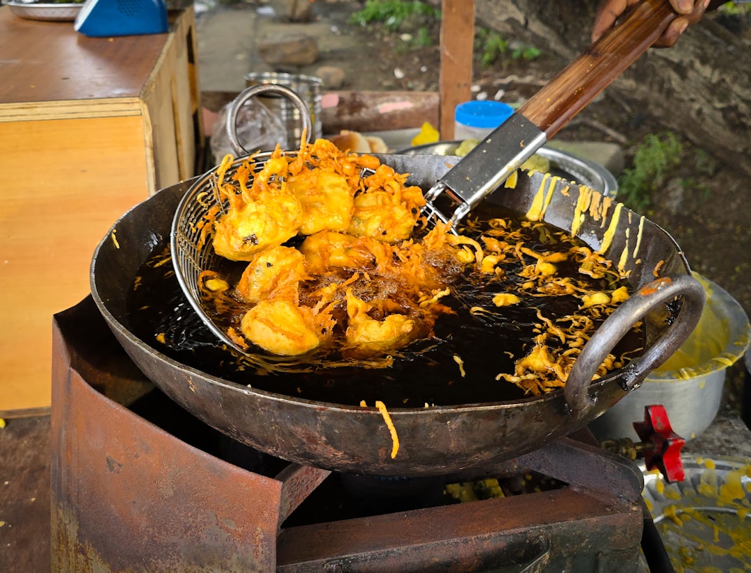 Raw chicken pieces being lowered into bubbling oil in a large pot with a thermometer visible