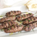 Lebanese kafta kebabs on metal skewers with perfect char marks, garnished with fresh parsley and served on a rustic wooden platter with grilled vegetables