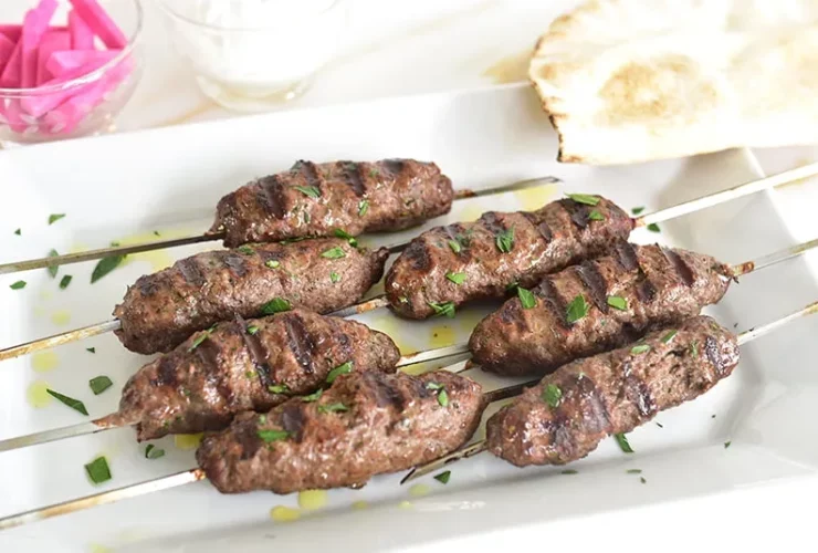 Lebanese kafta kebabs on metal skewers with perfect char marks, garnished with fresh parsley and served on a rustic wooden platter with grilled vegetables