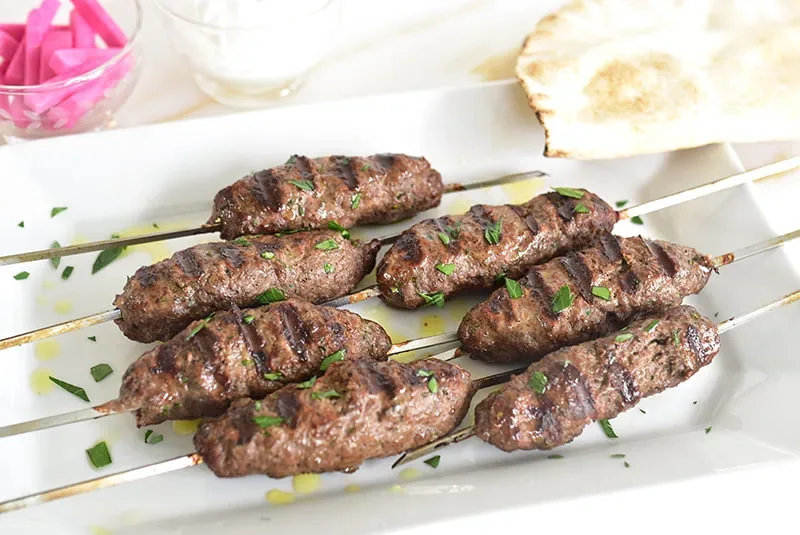 Lebanese kafta kebabs on metal skewers with perfect char marks, garnished with fresh parsley and served on a rustic wooden platter with grilled vegetables