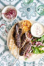 Close-up cross-section of a perfectly cooked kafta kebab showing the juicy interior with herbs and spices, alongside tahini sauce and fresh vegetables