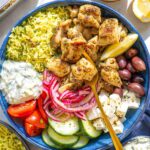 Mediterranean chicken bowl with golden herb-crusted chicken thighs, creamy tzatziki, colorful vegetables, and grains beautifully arranged in a rustic ceramic bowl