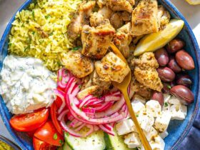 Mediterranean chicken bowl with golden herb-crusted chicken thighs, creamy tzatziki, colorful vegetables, and grains beautifully arranged in a rustic ceramic bowl