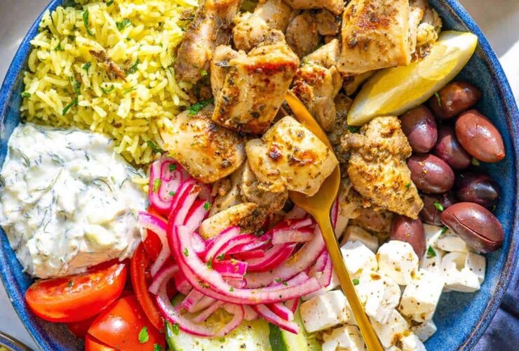 Mediterranean chicken bowl with golden herb-crusted chicken thighs, creamy tzatziki, colorful vegetables, and grains beautifully arranged in a rustic ceramic bowl