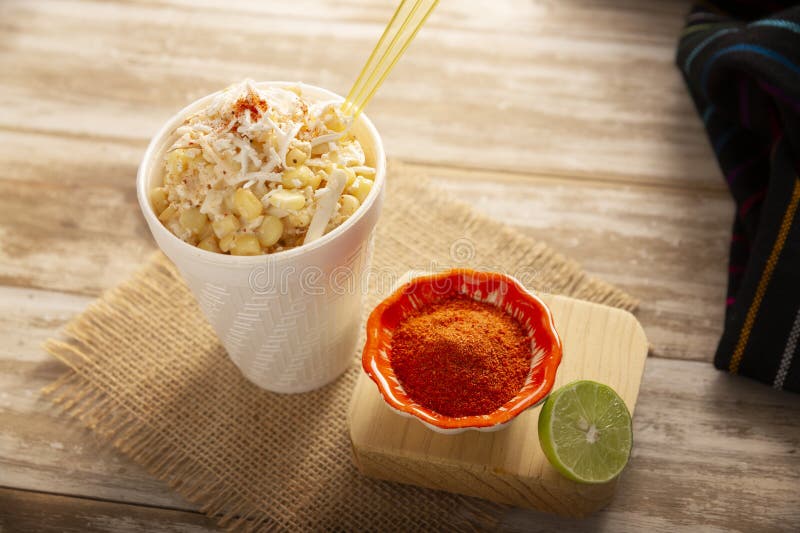 Extreme close-up of Mexican street corn kernels glistening with creamy sauce and topped with crumbled white cotija cheese and red chili powder, with a lime wedge in the background
