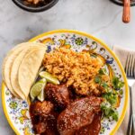 Mole poblano chicken served on white plate garnished with sesame seeds and cilantro with rice on the side