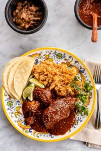 Mole poblano chicken served on white plate garnished with sesame seeds and cilantro with rice on the side