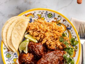 Mole poblano chicken served on white plate garnished with sesame seeds and cilantro with rice on the side
