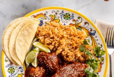 Mole poblano chicken served on white plate garnished with sesame seeds and cilantro with rice on the side