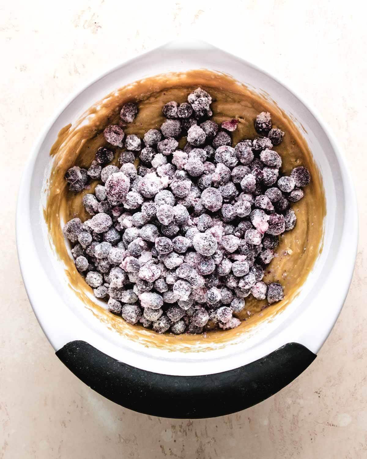 Step-by-step shot showing blueberries being tossed in flour and muffin batter being gently folded in a mixing bowl