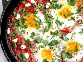 Shakshuka in cast iron skillet with golden runny egg yolks and fresh herbs, overhead shot with warm lighting