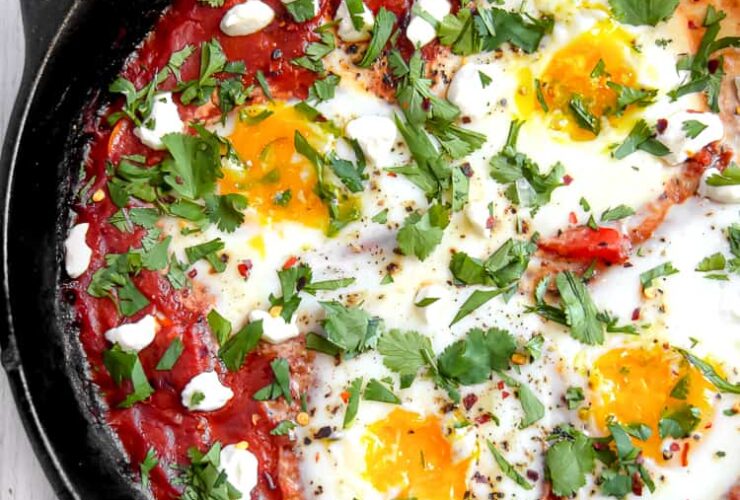 Shakshuka in cast iron skillet with golden runny egg yolks and fresh herbs, overhead shot with warm lighting
