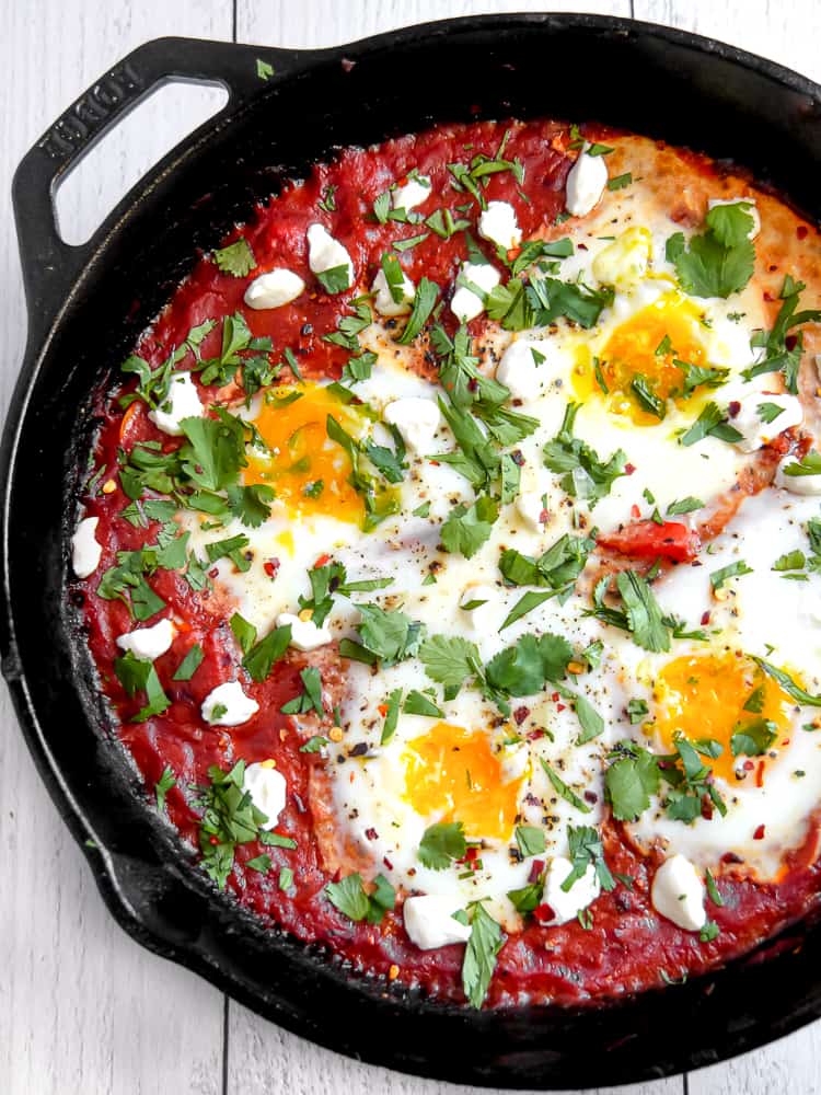 Shakshuka in cast iron skillet with golden runny egg yolks and fresh herbs, overhead shot with warm lighting