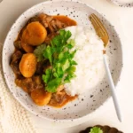 spicy shaved beef massaman curry in bowl with rice garnished with cilantro and lime