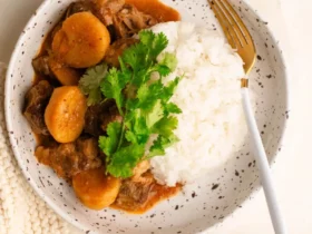 spicy shaved beef massaman curry in bowl with rice garnished with cilantro and lime