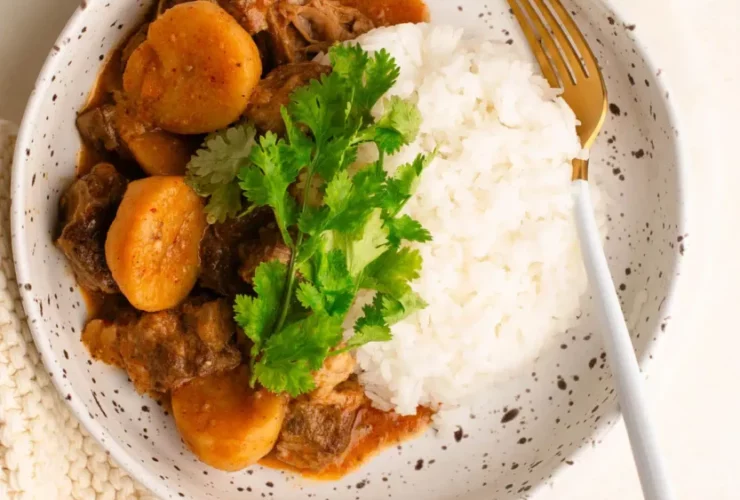 spicy shaved beef massaman curry in bowl with rice garnished with cilantro and lime
