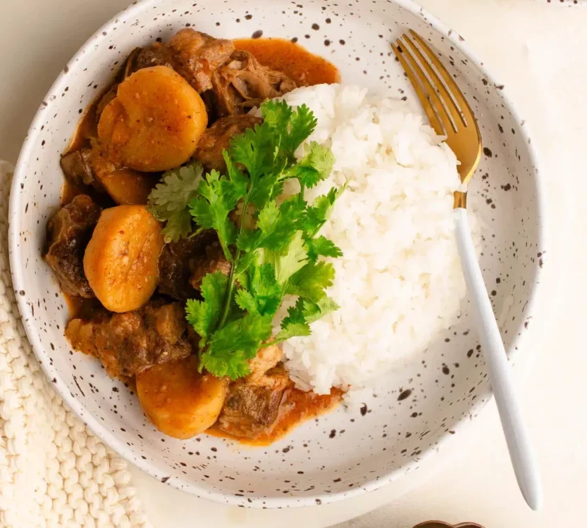 spicy shaved beef massaman curry in bowl with rice garnished with cilantro and lime