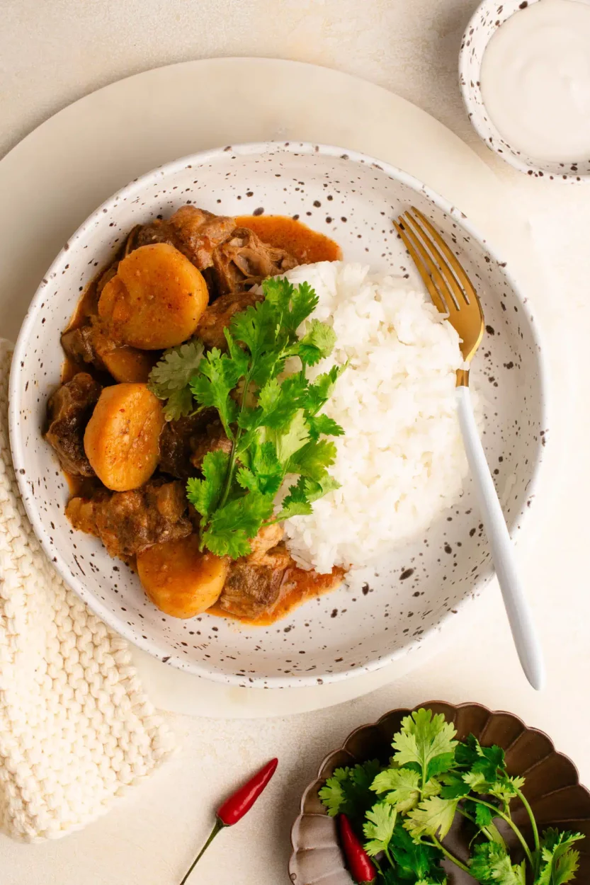 spicy shaved beef massaman curry in bowl with rice garnished with cilantro and lime