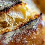 golden sourdough bread loaf with perfectly blistered crust and steam rising from a fresh slice, showing the beautiful open crumb structure