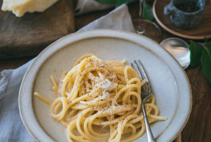 Spaghetti Carbonara served in a white ceramic bowl with freshly cracked black pepper and grated pecorino romano on top