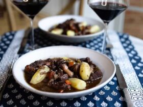 Beef Bourguignon served in rustic ceramic bowls with crusty bread, wine-dark sauce glistening, garnished with fresh herbs